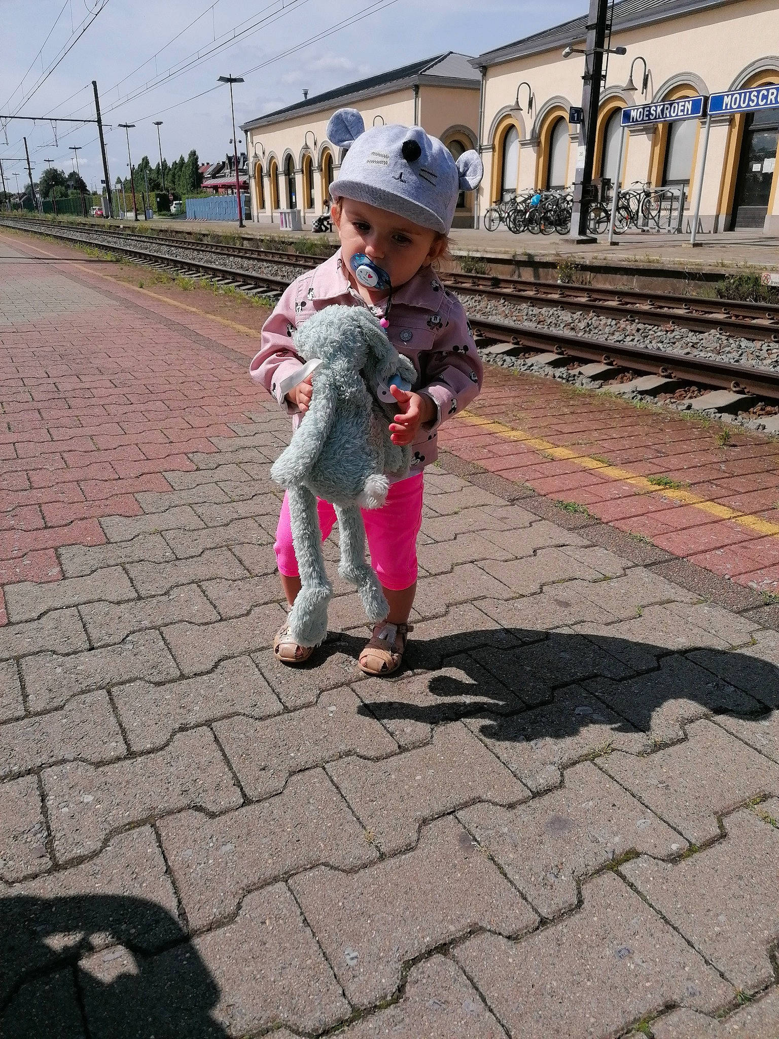Tyana a rejoint le concours — aidez-le/la à gagner de superbes lots ! asphalt, building, city, flooring, fun, grass, hat, headwear, leg, leisure, pedestrian, person, pink, road, road_surface, sidewalk, sky, sun_hat, temple, toddler