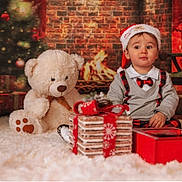Julian participe au concours pour gagner de l'argent avec cette photo : baby, carpet, child, christmas_tree, cozy, cute, decorations, festive, fireplace, gift, holiday, indoors, plaid, portrait, present, red, santa_hat, sitting, teddy_bear, white