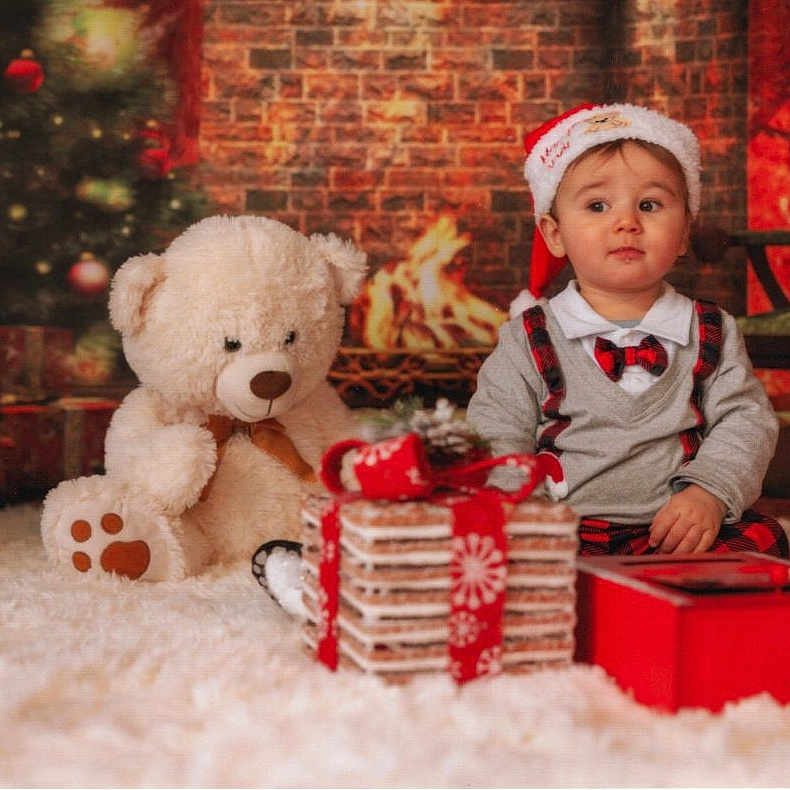 Julian participe au concours pour gagner de l'argent avec cette photo : baby, carpet, child, christmas_tree, cozy, cute, decorations, festive, fireplace, gift, holiday, indoors, plaid, portrait, present, red, santa_hat, sitting, teddy_bear, white