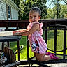 Isabella is registered to the contest to win money with this photo: toddler, child, girl, pink_dress, minnie_mouse, chair, deck, outdoor, sunlight, greenery, grass, trees, house, smile, kneeling, metal_furniture, summer, cute, portrait, daytime