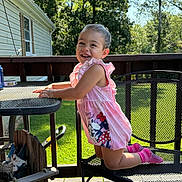 Isabella is registered to the contest to win money with this photo: toddler, child, smile, pink_clothing, outdoor, deck, metal_chair, table, sunlight, greenery, house, happy, playful, summer, daylight, railing, shadows, socks, young_child, balancing