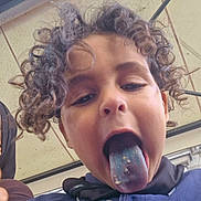 Emanallah a rejoint le concours — aidez-le/la à gagner de superbes lots ! child, curly_hair, blue_tongue, crumbs, playful, face, tongue_out, casual_clothing, buttoned_shirt, outdoor, roof, mischievous, close_up, young, person, portrait, fun, expression, head, daylight