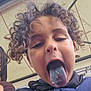 child, curly_hair, blue_tongue, crumbs, playful, face, tongue_out, casual_clothing, buttoned_shirt, outdoor, roof, mischievous, close_up, young, person, portrait, fun, expression, head, daylight