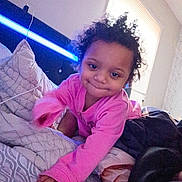 Kataleya is registered to the contest to win money with this photo: toddler, child, pink_clothing, bed, bedding, pillow, blanket, crawling, smile, curly_hair, indoors, window, natural_light, blue_light, head, hand, person, cute, cozy, room