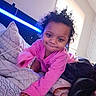 toddler, child, pink_clothing, bed, bedding, pillow, blanket, crawling, smile, curly_hair, indoors, window, natural_light, blue_light, head, hand, person, cute, cozy, room