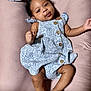 baby, infant, child, dress, patterned_clothing, wooden_buttons, lying_down, pink_background, curly_hair, smiling, cute, skin, hand, foot, portrait, indoors, soft_texture, fabric, closeup, person