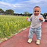 Ali a rejoint le concours — aidez-le/la à gagner de superbes lots ! casual_clothing, child, clouds, cute, daylight, grass, happy, nature, outdoor, pants, park, pathway, people_in_background, shoes, sky, smiling, standing, striped_shirt, toddler, trees