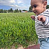 toddler, child, walking, outdoor, grass, field, sky, clouds, striped_shirt, pants, shoes, path, greenery, nature, young_child, side_view, person, cute, determined, daytime