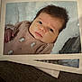 baby, newborn, infant, portrait, printed_photo, paper, blanket, pajamas, hair, face, eyes, hand, closeup, studio_style, border, table, cozy, soft_texture, photograph, sleepy