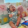 baby, child, smiling, laughing, bow, plush_toy, book, quilt, couch, colorful, indoor, window, sunshine, happy, infant, clothing, daisy_pattern, person, portrait, playful