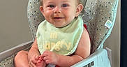 Paisley is registered to the contest to win money with this photo: baby, high_chair, bib, smile, child, infant, happy, indoor, foot, hand, face, clothing, seat, person, young_child, cute, expression, playful, home, furniture