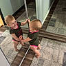 Paisley is registered to the contest to win money with this photo: toddler, child, mirror, reflection, barefoot, curious, indoor, carpet, floor, wood_floor, wall, short_hair, onesie, baby, smiling, standing, home, room, playful, person