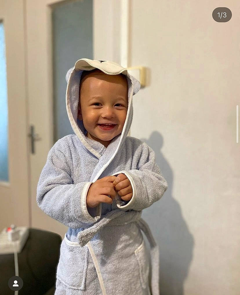 Tyméo participe au concours pour gagner de l'argent avec cette photo : baby, baby_toddler_clothing, cap, child, face, fashion_accessory, fun, gesture, happy, hat, headwear, hoodie, human_body, joy, laugh, person, room, sitting, sleeve, smile