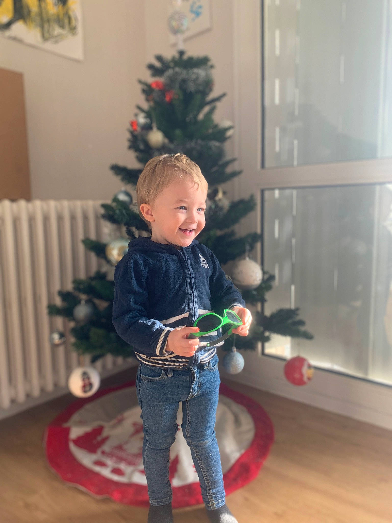 Tyméo participe au concours pour gagner de l'argent avec cette photo : child, christmas_decoration, christmas_eve, christmas_ornament, christmas_tree, conifer, event, flooring, happy, hardwood, holiday, holiday_ornament, jeans, joy, ornament, person, plant, smile, toddler, toy
