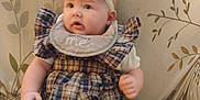 Luna is registered to the contest to win money with this photo: baby, child, plaid_dress, headband, bib, sitting, couch, floral_pattern, curious, indoors, soft_lighting, cute, infant, clothing, footwear, pink_socks, portrait, person, young_child, comfortable