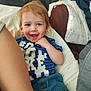 toddler, child, smiling, happy, blue_shirt, jeans, indoor, casual, portrait, person, light_hair, face, sitting, home, couch, blanket, fabric, comfort, relaxed, cute