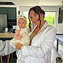 woman, baby, child, smile, dress, headband, white_blazer, indoor, kitchen, cat, furniture, table, chair, window, natural_light, floor, person, holding, happy, portrait
