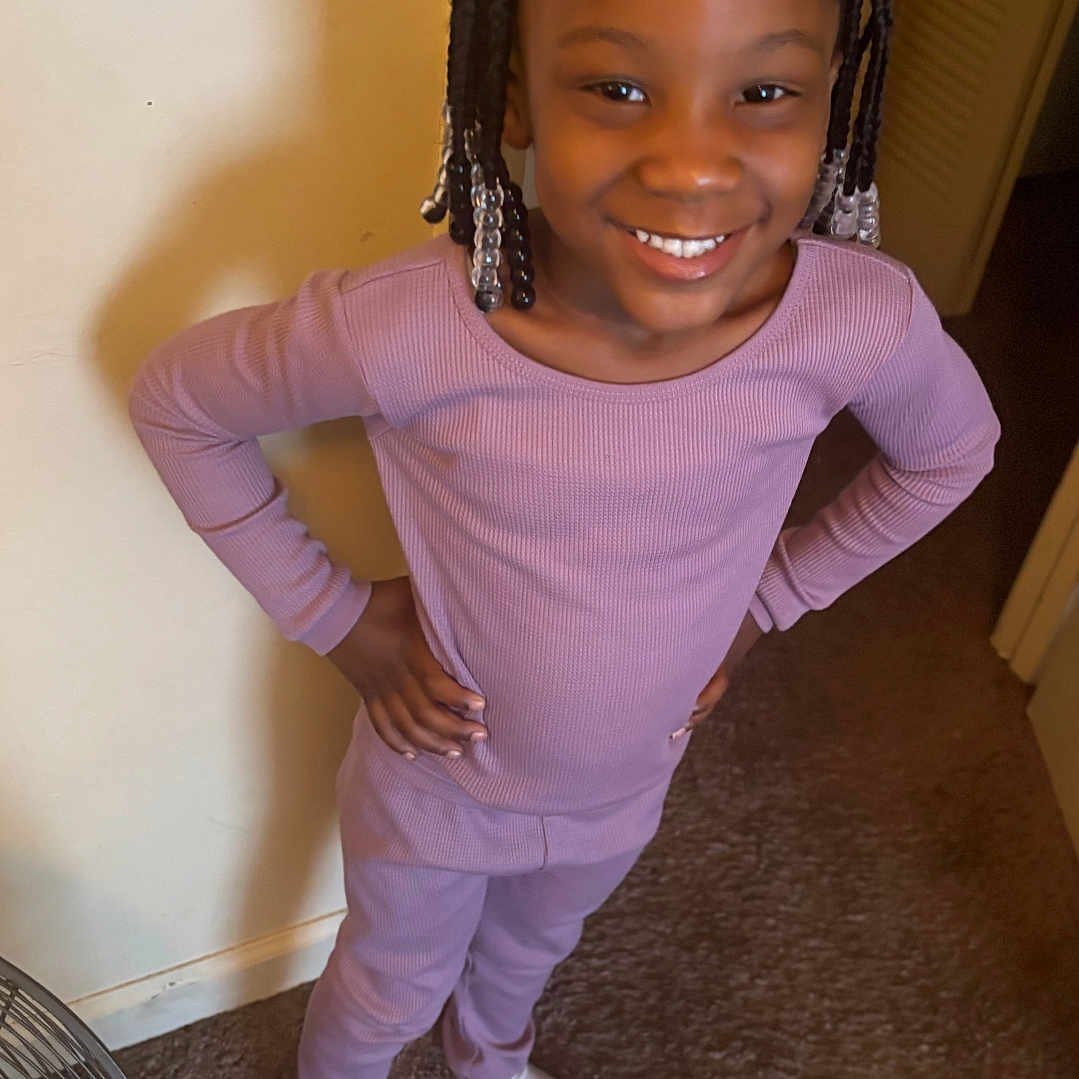 Elliana joined the competition — help win amazing prizes! beads, braided_hair, carpet, child, door, fan, girl, hands_on_hips, happy, home, indoor, pajamas, person, portrait, purple_clothing, smiling, socks, standing, unicorn, wall