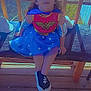Harlee is registered to the contest to win money with this photo: child, wonder_woman_costume, superhero, blue_skirt, headband, cape, bench, wooden_floor, sunlight, shadows, toy, helmet, smile, outdoor, costume, sitting, footwear, armbands, portrait, playful