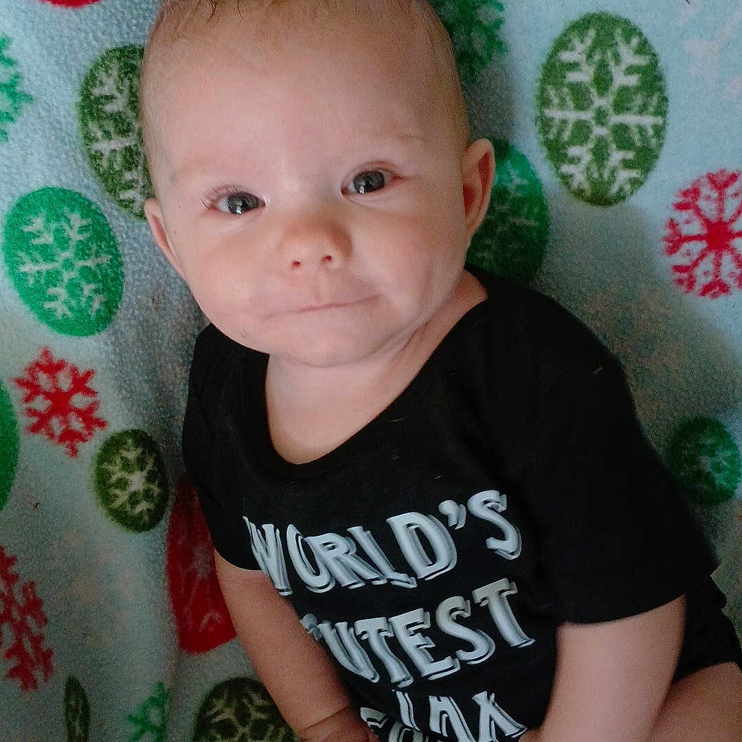 Charles Jaxson joined the competition — help win amazing prizes! baby, black_clothing, blanket, blue, child, cute, face, green, hand, head, indoors, infant, onesie, pattern, portrait, red, sitting, skin, smiling, snowflake