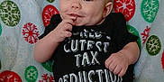 Charles Jaxson is registered to the contest to win money with this photo: baby, bare_feet, black_clothing, blanket, cheeks, child, cute, green, hand_near_mouth, happy, holiday_theme, indoors, infant, onesie, portrait, red, sitting, smiling, snowflake_pattern, white