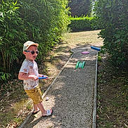Noah participe au concours pour gagner de l'argent avec cette photo : child, boy, sunglasses, cap, mini_golf, golf_club, golf_ball, gravel_path, greenery, bushes, sunny_day, shorts, tshirt, footwear, outdoor, playing, recreation, summer, nature, leisure