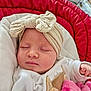 baby, sleeping, headband, bow, blanket, red_cushion, white_clothing, infant, soft_toy, peaceful, cute, close_up, indoors, child, person, resting, cozy, newborn, pink, comfort
