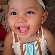 Novanny Charles is registered to the contest to win money with this photo: baby, child, smiling, happy, face, headband, bow, earrings, necklace, dress, striped_clothing, indoors, person, cute, portrait, young_child, jewelry, closeup, skin, hand