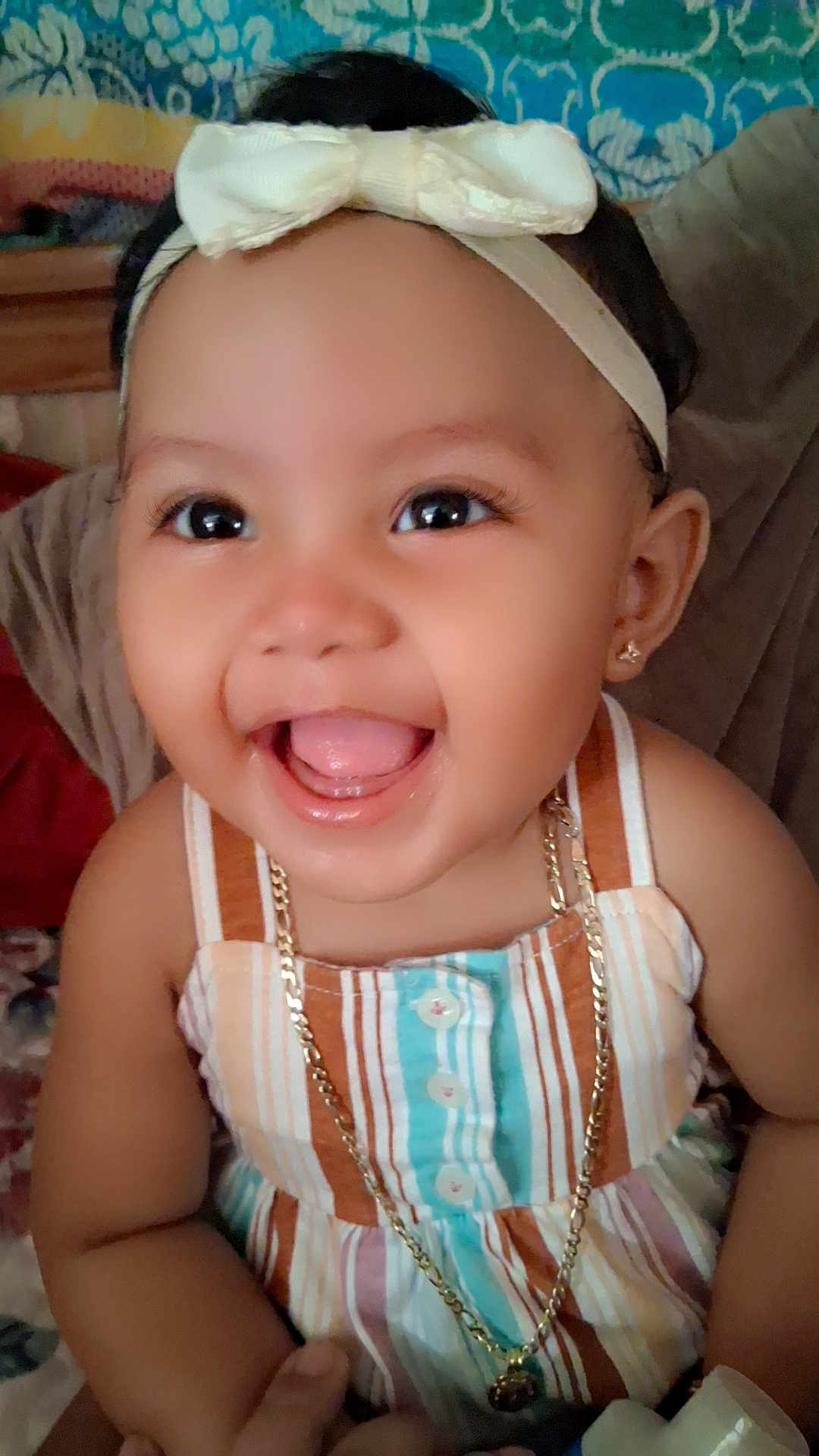 Novanny Charles is registered to the contest to win money with this photo: baby, child, smiling, happy, face, headband, bow, earrings, necklace, dress, striped_clothing, indoors, person, cute, portrait, young_child, jewelry, closeup, skin, hand
