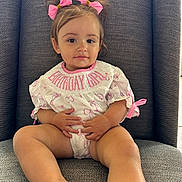 Mila joined the competition — help win amazing prizes! toddler, child, girl, birthday_girl, pink_bows, hair_accessories, white_outfit, sitting, gray_chair, cushion, indoors, portrait, cute, smiling, hands, legs, face, eyes, young_child, comfortable