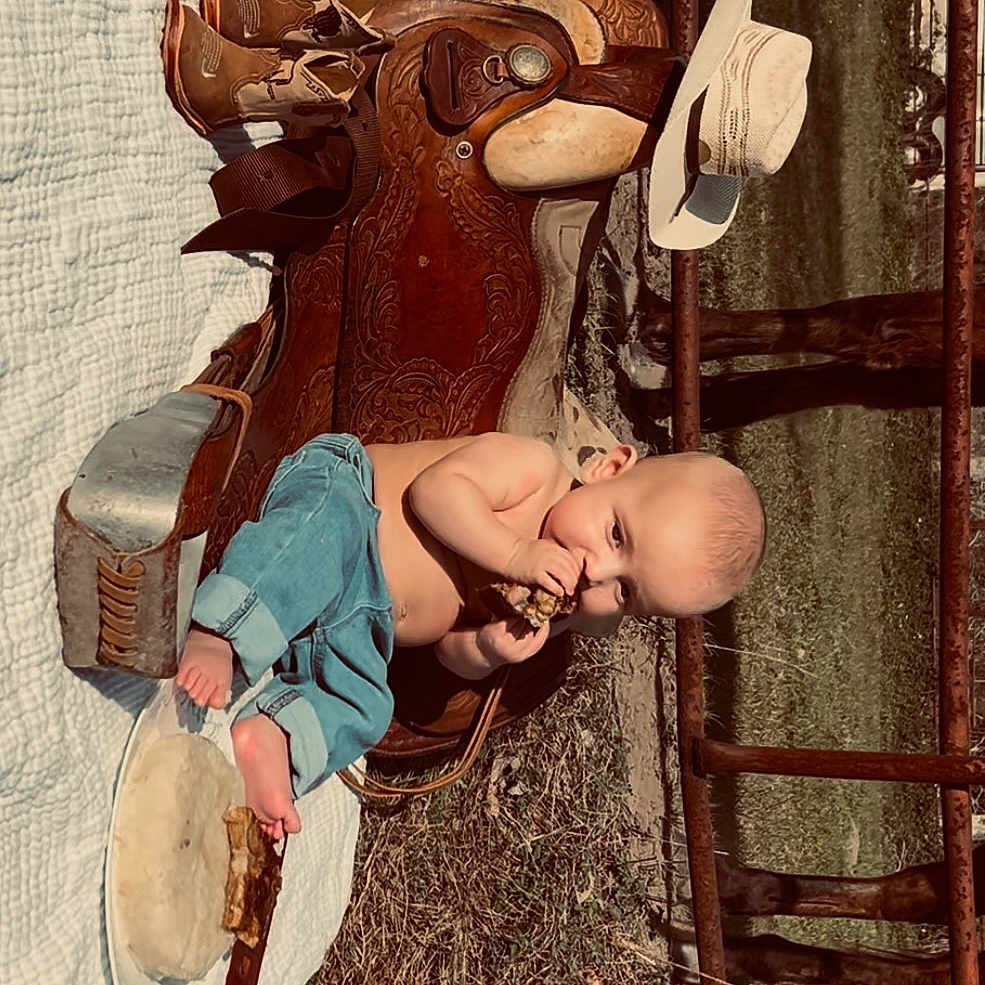 James is registered to the contest to win money with this photo: baby, baseball, baseballglove, chair, clothing, face, footwear, furniture, glove, hat, head, pants, person, photography, portrait, sandal, shoe, sitting, sport, wood