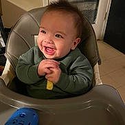Riot is registered to the contest to win money with this photo: baby, child, high_chair, smile, happy, indoor, toy, green_sweater, hands, mouth_open, face, chair, plastic_tray, kitchen, door, floor_tile, evening, snack, playtime, cute