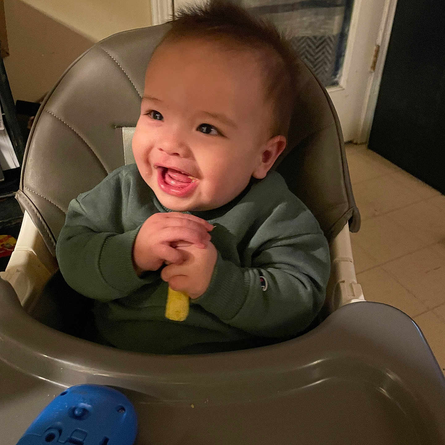 Riot is registered to the contest to win money with this photo: baby, chair, child, cute, door, evening, face, floor_tile, green_sweater, hands, happy, high_chair, indoor, kitchen, mouth_open, plastic_tray, playtime, smile, snack, toy