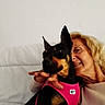 Lou participe au concours pour gagner de l'argent avec cette photo : woman, dog, doberman, black_and_tan, pet, cuddle, smiling, portrait, indoor, couch, white_cushion, pink_harness, pointed_ears, short_hair, human_face, dog_face, sitting, companionship, home, photograph