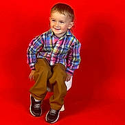Noah Lee joined the competition — help win amazing prizes! toddler, child, smiling, plaid_shirt, brown_pants, black_shoes, sitting, chair, red_background, indoor, happy, cute, portrait, fashion, casual_clothing, young_child, studio, colorful, footwear, person