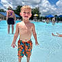 Noah Lee is registered to the contest to win money with this photo: child, boy, swim_trunks, water, pool, outdoor, summer, sunny, sky, clouds, people, umbrella, barefoot, smiling, shallow_water, recreation, vacation, fun, daytime, leisure