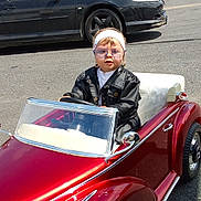 Marbella a rejoint le concours — aidez-le/la à gagner de superbes lots ! accessory, black_car, child, fashion, fence, glasses, greenery, headband, leather_jacket, outdoor, person, red_car, road, seat, street, sunny, toddler, toy_car, vehicle, wheel