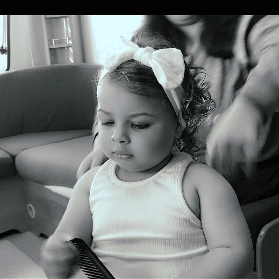Marbella participe au concours pour gagner de l'argent avec cette photo : baby, black_and_white, bow, child, comb, couch, curly_hair, cute, focused, furniture, hand, headband, home, indoor, person, portrait, seated, soft_lighting, toddler, white_tank_top