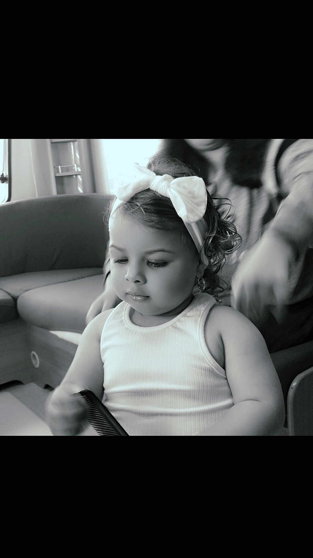 Marbella participe au concours pour gagner de l'argent avec cette photo : child, toddler, bow, headband, comb, indoor, couch, person, curly_hair, white_tank_top, furniture, cute, black_and_white, portrait, baby, hand, seated, focused, home, soft_lighting