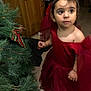 celebration, child, christmas_tree, curious, cute, decorations, dressed_up, event, face, festive, greenery, holiday, holiday_season, indoor, person, portrait, red_dress, toddler, tree, young_child