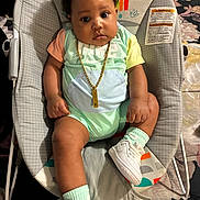 Dahari is registered to the contest to win money with this photo: baby, child, infant, baby_rocker, onesie, sneakers, socks, gold_chain, curly_hair, indoor, cushion, patterned_blanket, monkey_print, cute, chubby_cheeks, seated, portrait, wide_eyes, colorful_clothing, comfortable