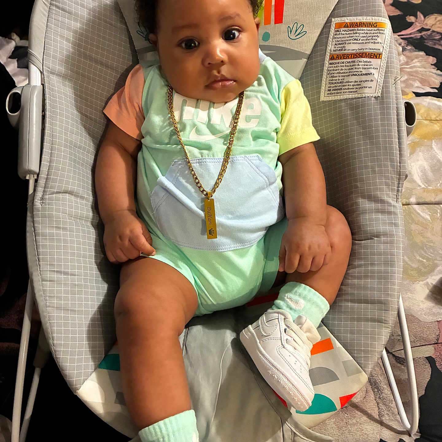 Dahari is registered to the contest to win money with this photo: baby, child, infant, baby_rocker, onesie, sneakers, socks, gold_chain, curly_hair, indoor, cushion, patterned_blanket, monkey_print, cute, chubby_cheeks, seated, portrait, wide_eyes, colorful_clothing, comfortable