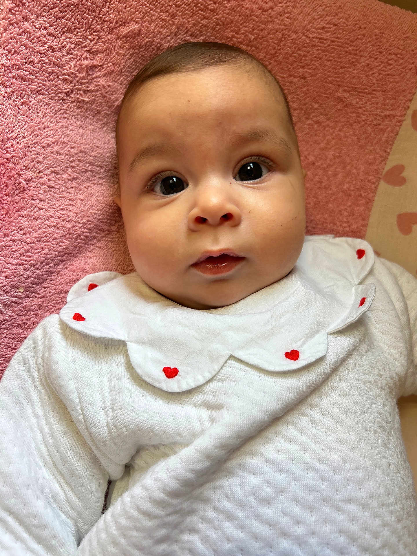 Tesnim participe au concours pour gagner de l'argent avec cette photo : baby, infant, face, eyes, white_clothing, heart_pattern, pink_towel, cute, portrait, child, soft_texture, closeup, adorable, young, laying_down, expression, skin, head, mouth, indoor