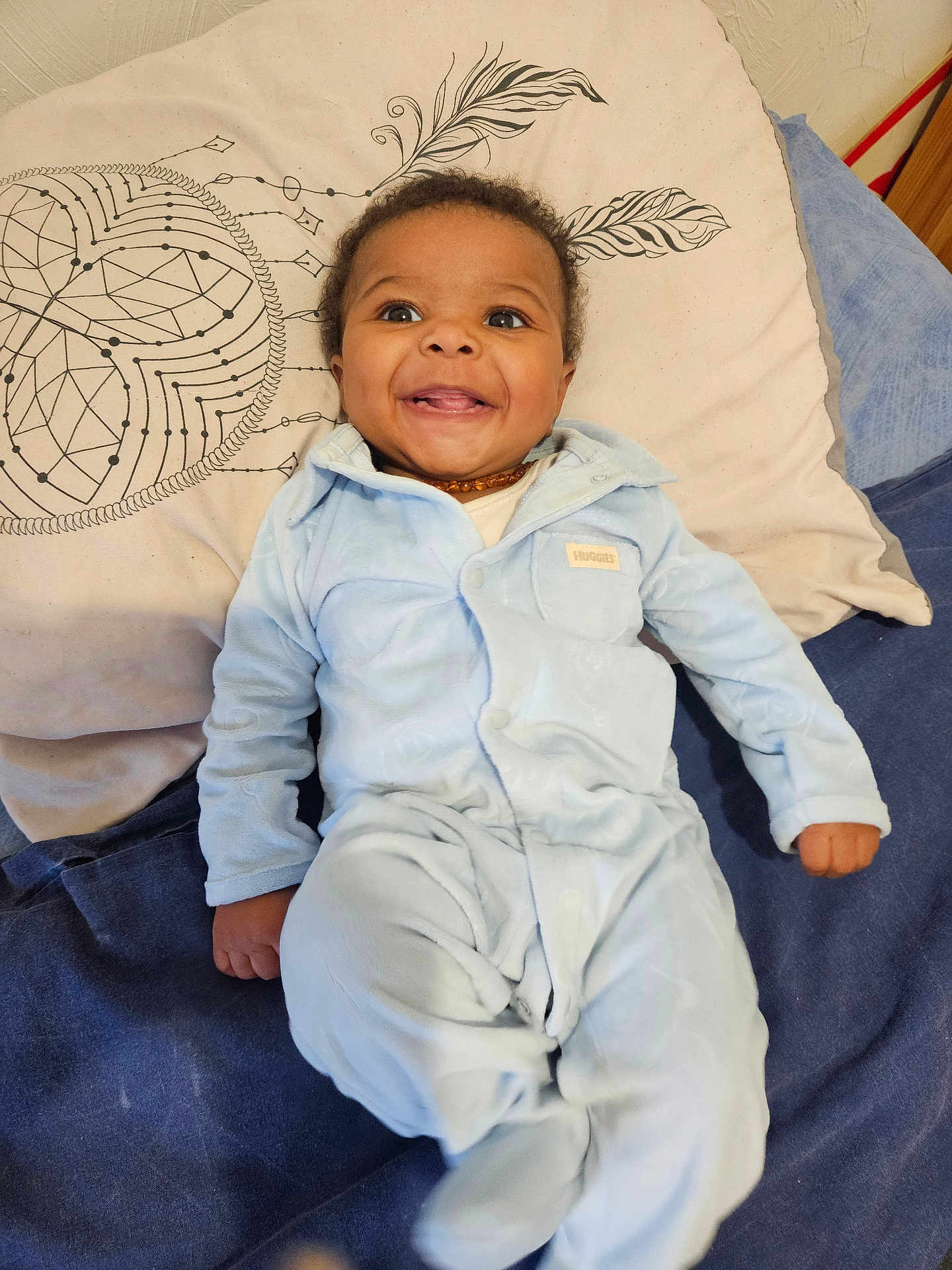 Makan a rejoint le concours — aidez-le/la à gagner de superbes lots ! baby, infant, child, smile, happy, pajamas, blue_pajamas, onesie, pillow, bedding, blanket, lying_down, face, eyes, hands, feet, amber_necklace, indoor, portrait, cute
