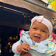 Mountabih Garrami joined the competition — help win amazing prizes! baby, child, smiling, headband, bib, mickey_mouse, hand, person, outdoor, building, flag, clothing, happy, portrait, cute, infant, holding, face, colorful, joyful