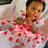 baby, child, infant, girl, dress, pink, strawberry, bow, hair_accessory, smiling, cute, sitting, foot, hand, clothing, soft_toy, blanket, indoors, portrait, happy