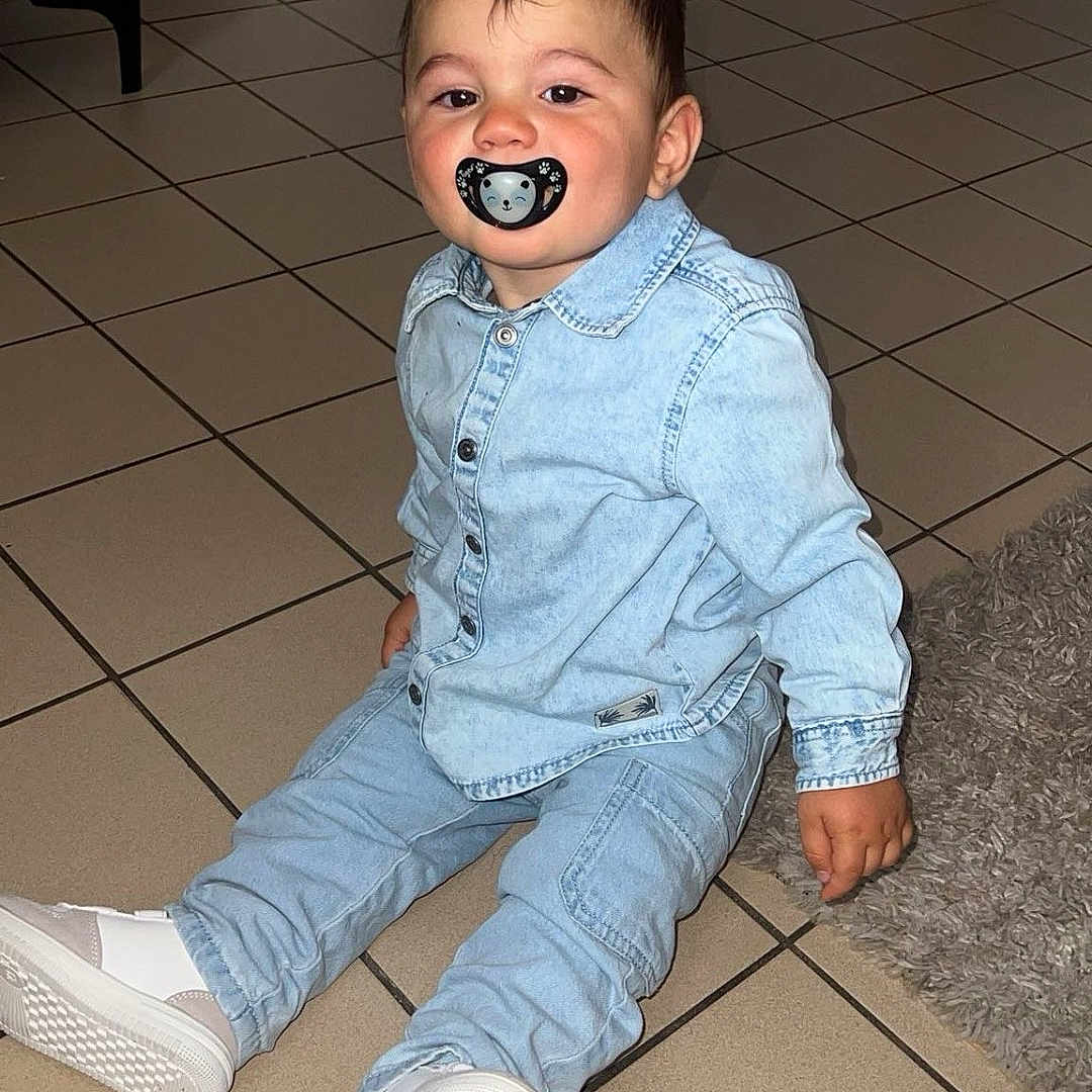 Thiméo a rejoint le concours — aidez-le/la à gagner de superbes lots ! baby, casual, child, curious, cute, denim_outfit, expression, face, floor, footwear, furniture, hair, home, indoor, pacifier, rug, seated, tile, toddler, white_shoes