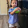 child, toddler, girl, portrait, standing, smiling, ball, toy, dress, shorts, sneakers, hair_bows, indoor, living_room, couch, wood_floor, birthday, balloons, colorful, fashion