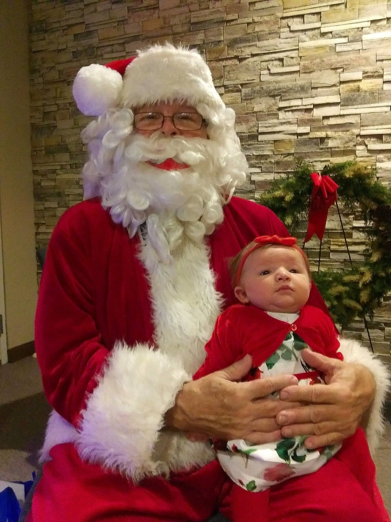 Joy is registered to the contest to win money with this photo: baby, beard, christmas, christmas_eve, costume, costume_accessory, costume_hat, event, facial_hair, fictional_character, fur, fur_clothing, hat, holiday, human, human_body, lap, moustache, person, red