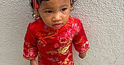 Aviora is registered to the contest to win money with this photo: child, toddler, portrait, standing, red_outfit, floral_pattern, traditional_clothing, headpiece, hair_ornament, jewelry, face, serious_expression, indoor, textured_wall, tile_floor, shoes, fashion, cultural_attire, full_body, photography